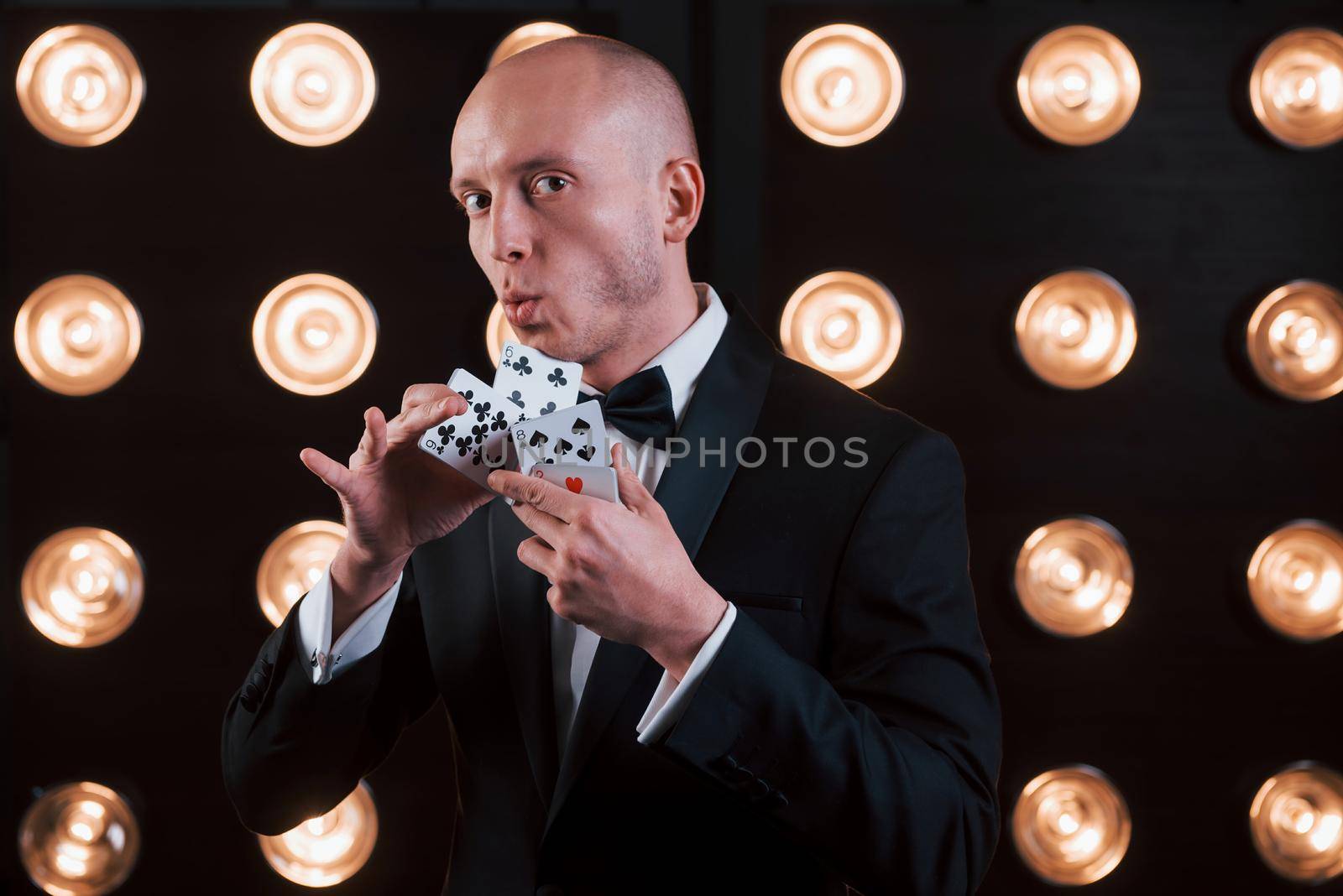 This gonna impress you. Magician in black suit and with playing cards standing in the room with special lighting at backstage.