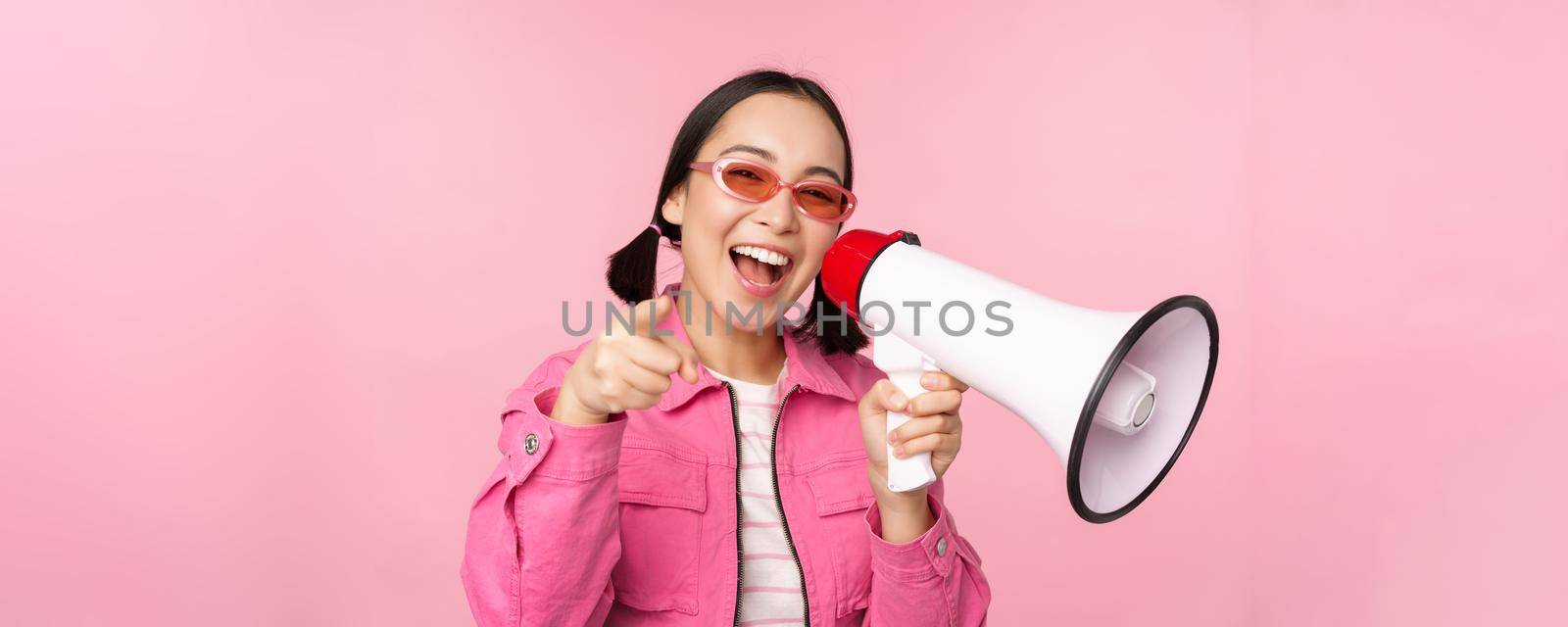 Attention, announcement concept. Enthusiastic asian girl shouting in megaphone, advertising with speaker, recruiting, standing over pink background.