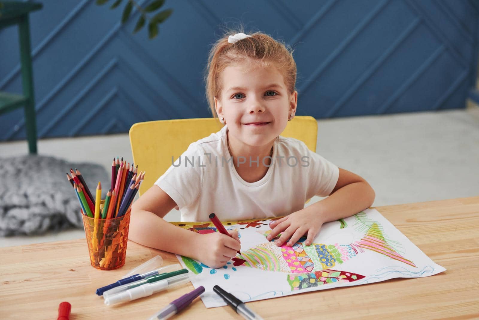 Cute little girl in art school draws her first paintings by pencils and markers.