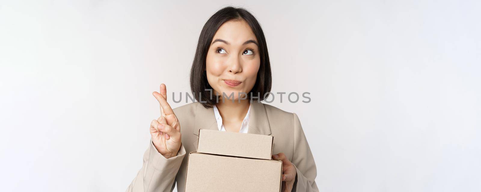 Hopeful asian entrepreneur, business woman holding boxes with customer order, making wish, wishing and anticipating, standing over white background.