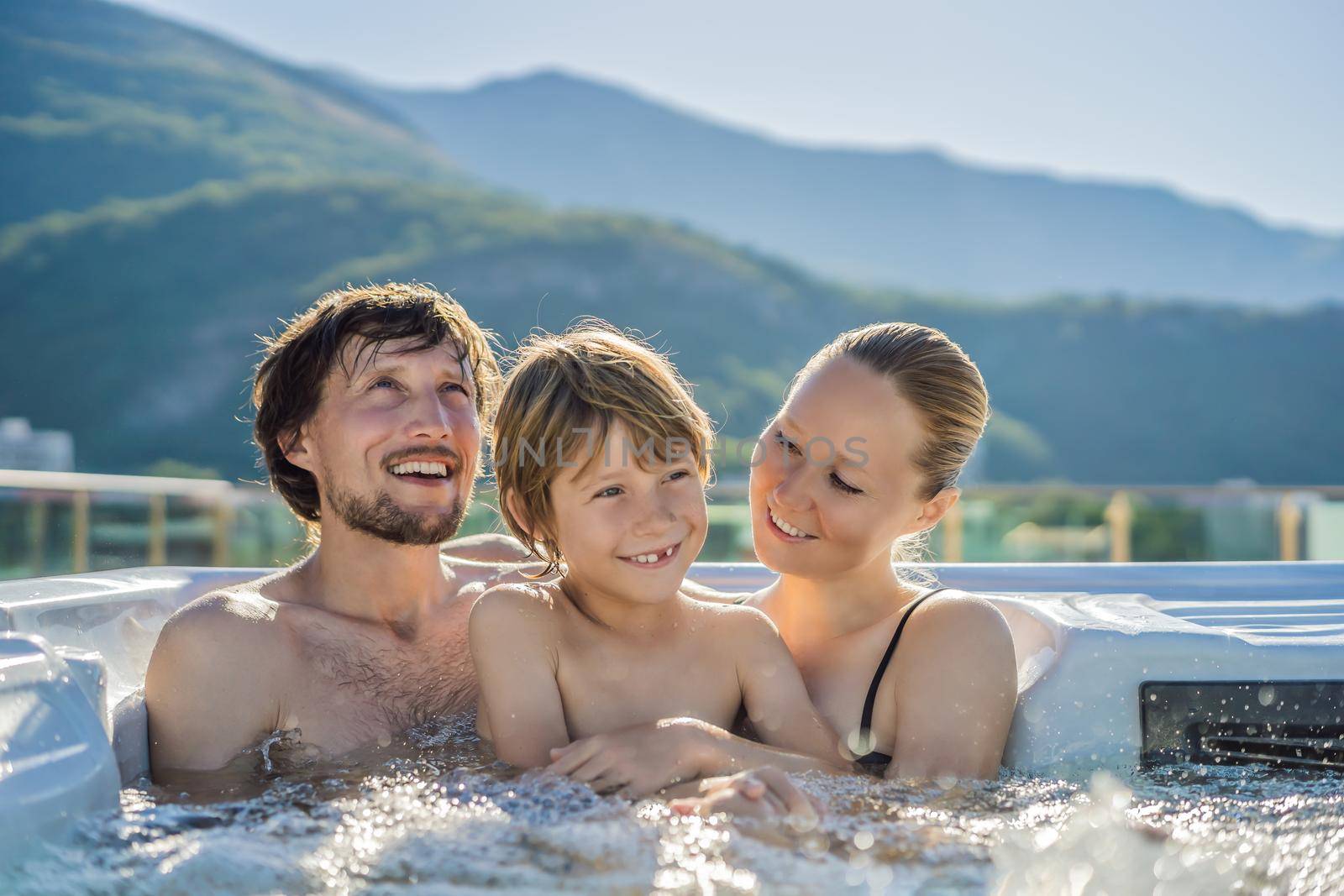 Portrait of young carefree happy smiling happy family relaxing at hot tub during enjoying happy traveling moment vacation. Life against the background of green big mountains.