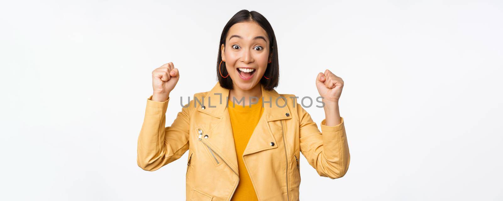 Image of asian woman dancing and smiling happy, celebrating victory, triumphing, standing over white background. copy space