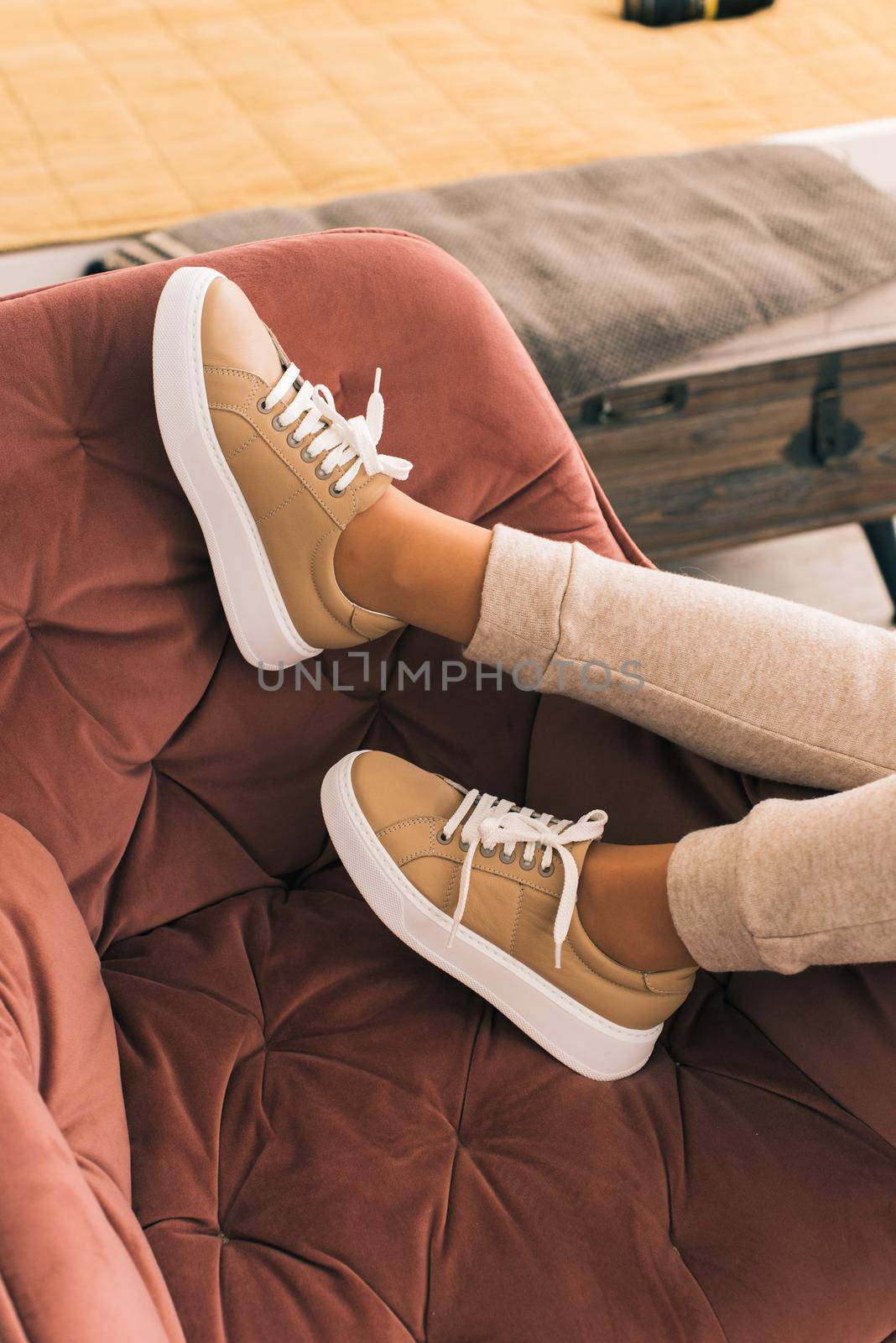 photo of a women legs in beige sports suit and stylish leather sneakers posing in the chair. selective focus. Indoors