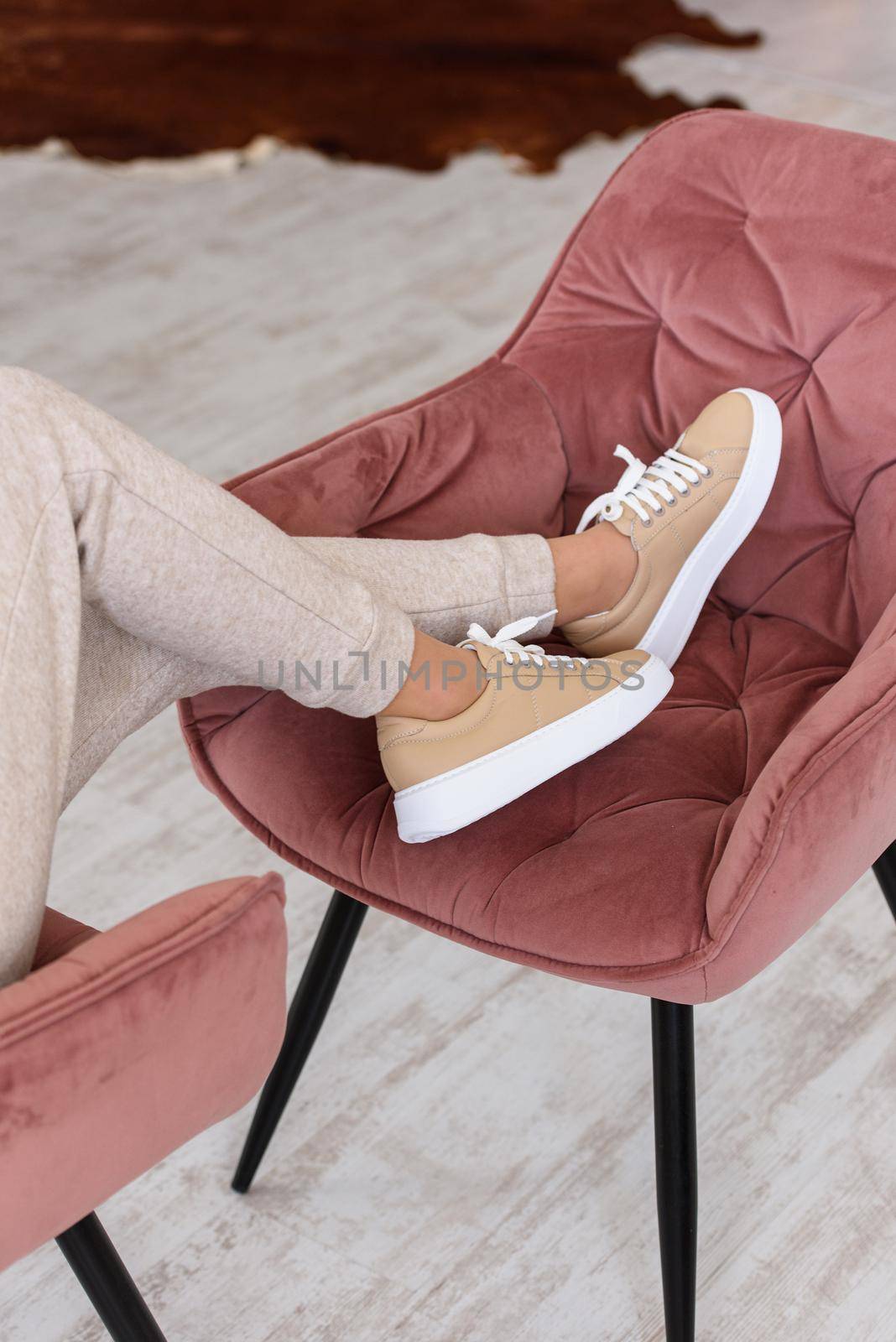 photo of a women legs in beige sports suit and stylish leather sneakers posing in the chair. selective focus. Indoors
