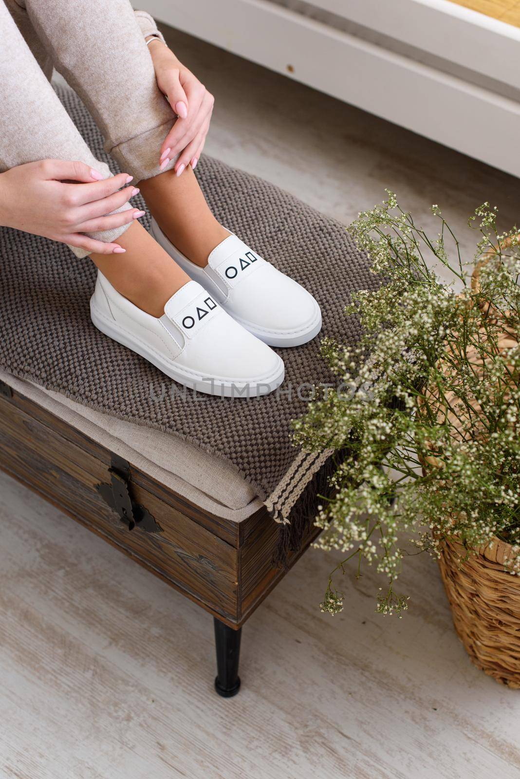 photo of a womens legs in beige sports suit and stylish white leather sneakers posing on a bench. selective focus. Indoors