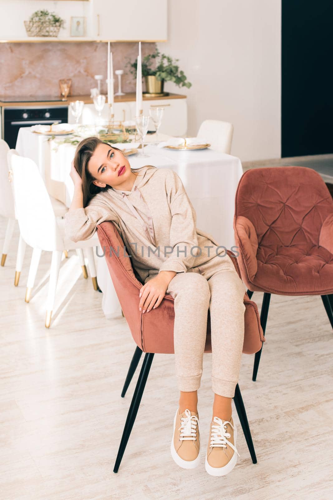 photo of a women in beige sports suit and stylish leather sneakers posing in the chair on a kitchen . selective focus. Indoors