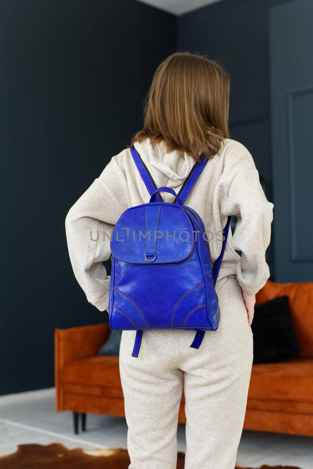 photo of a women in beige sports suit and blue leather backpack posing in a hotel room. selective focus. Indoors