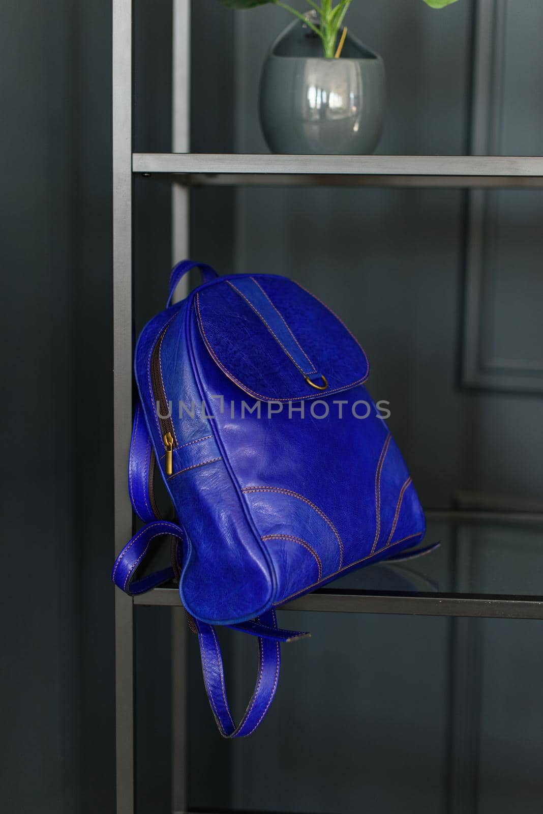 A deep blue leather modern backpack on a shelf. Indoors