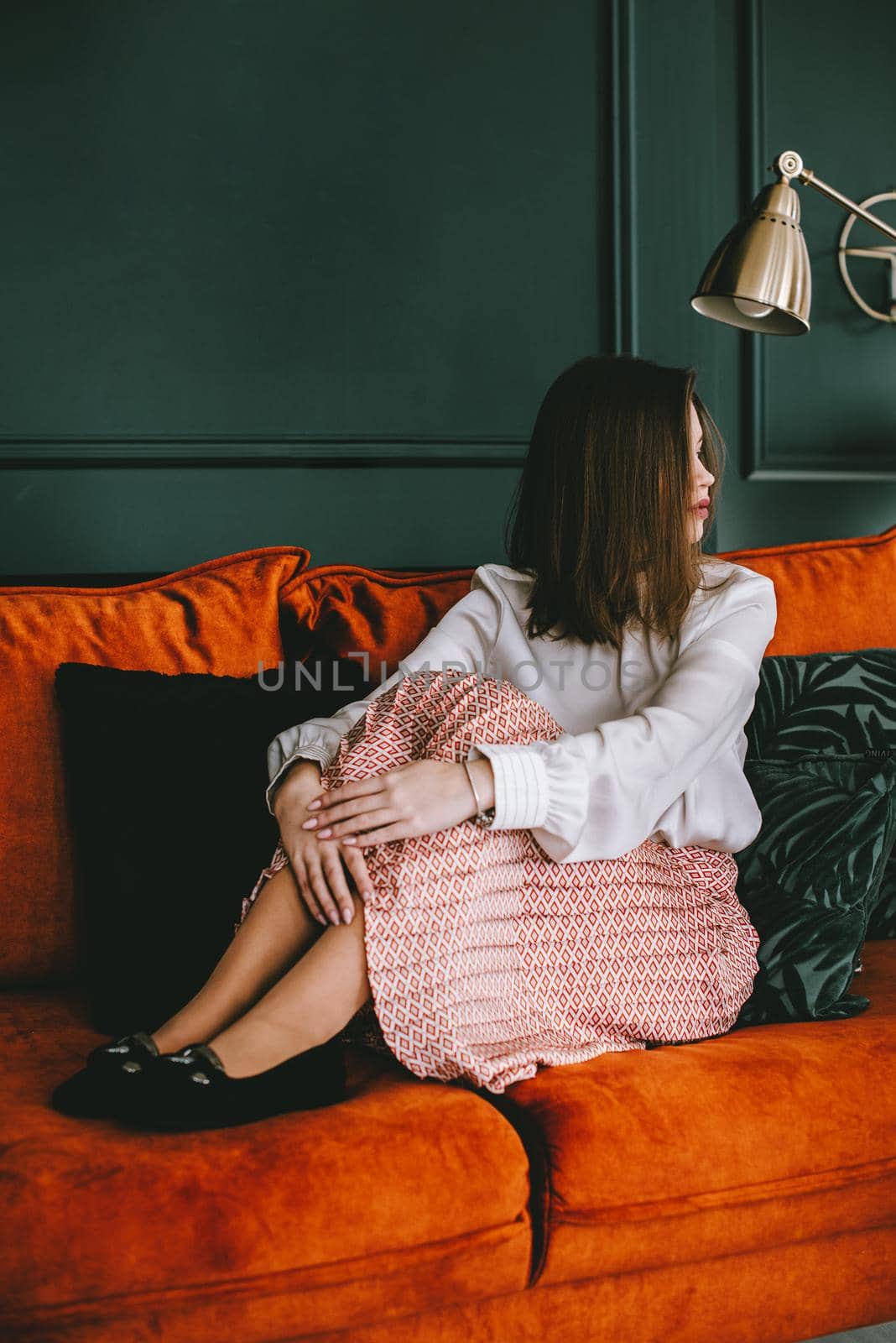 Portrait of fashionable young woman in a beige skirt, white blouse and stylish beige black seude shoes with a buckle posing on a orange sofa. by Ashtray25