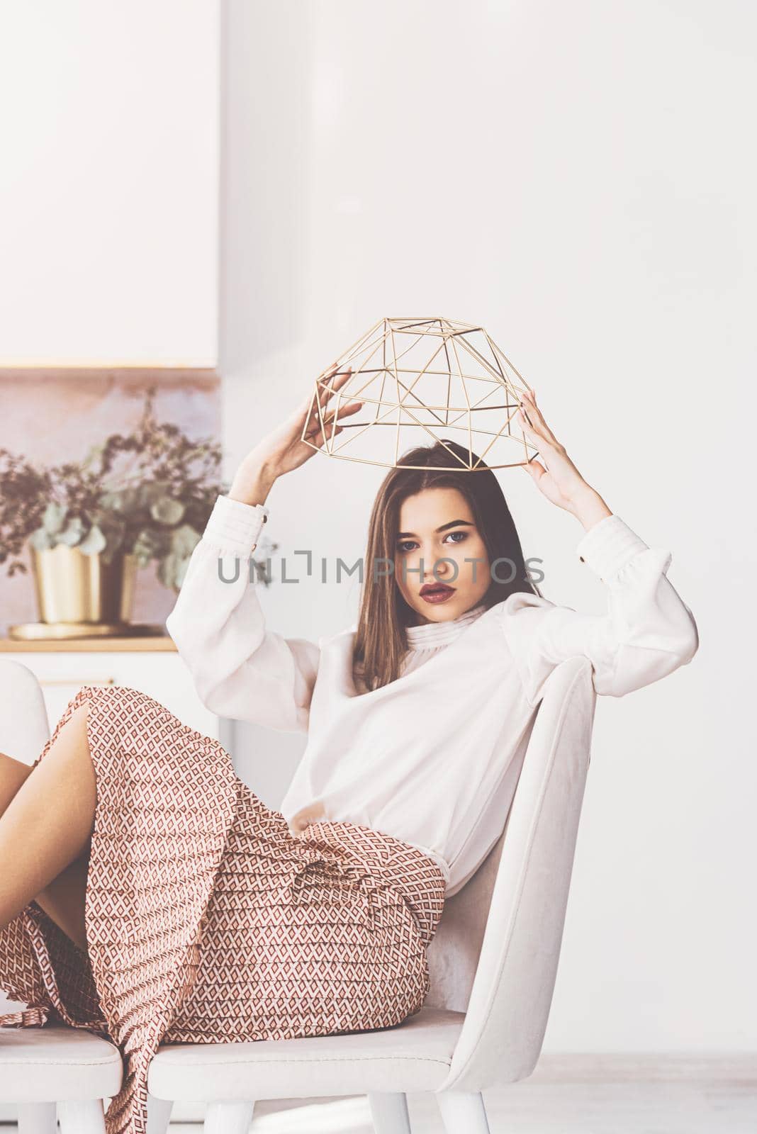 Portrait of fashionable women in beige skirt and white blouse posing on the kitchen in a chair. Girl with a big red lips