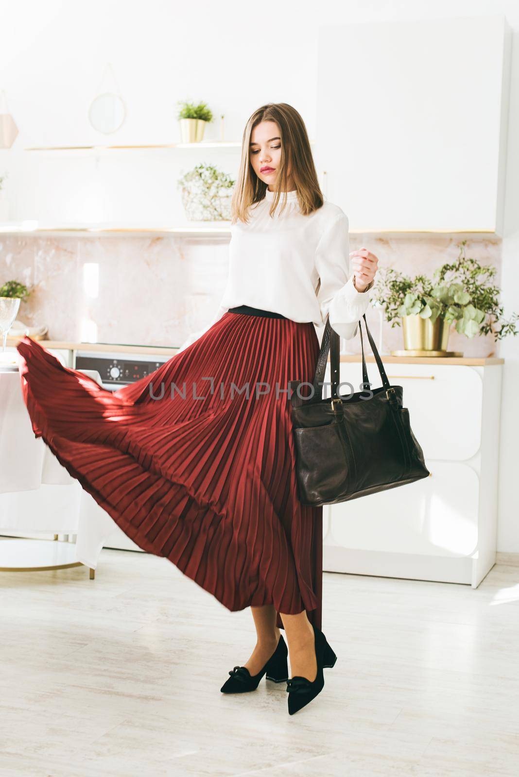 Portrait of fashionable women in a red skirt, white blouse and stylish suede shoes with a buckle posing on the kitchen. Girl with a big red lips