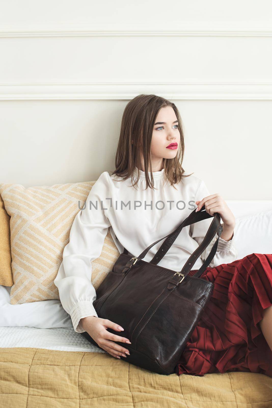 Portrait of fashionable women in red skirt, white blouse posing in a bed. Girl with a big red lips