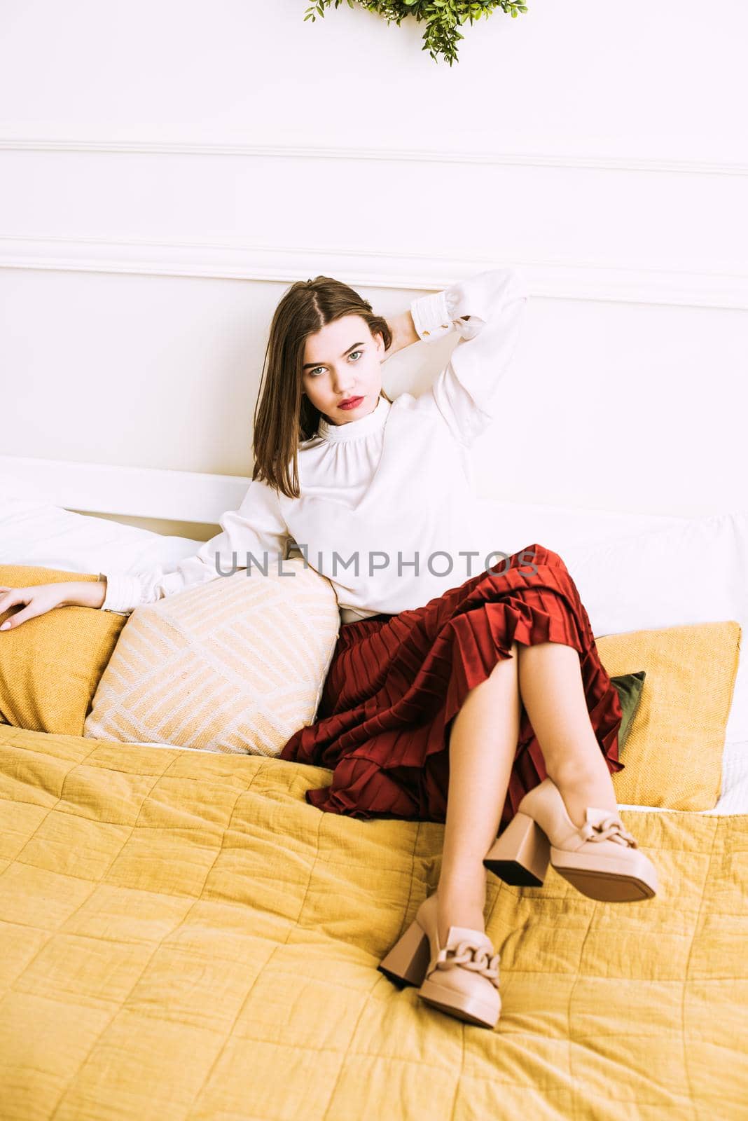 Portrait of fashionable women in red skirt, white blouse and stylish beige high-heeled shoes with a chain buckle posing in a bed by Ashtray25