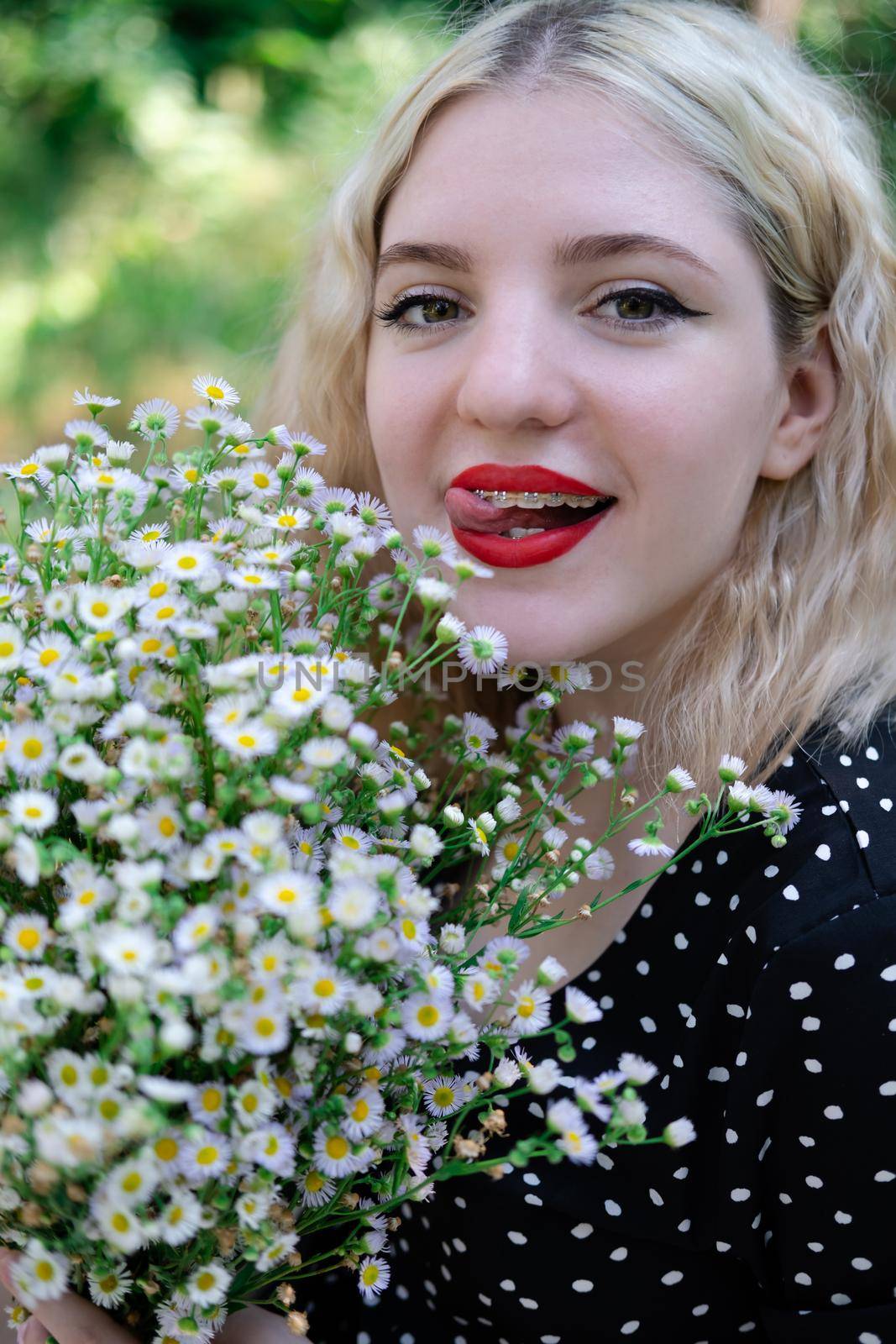 portrait of a charming blonde teenage girl wearing teeth braces with bouquet of white wildflowers. female with braces in mouth. healthy teeth. orthodontist dentist by oliavesna