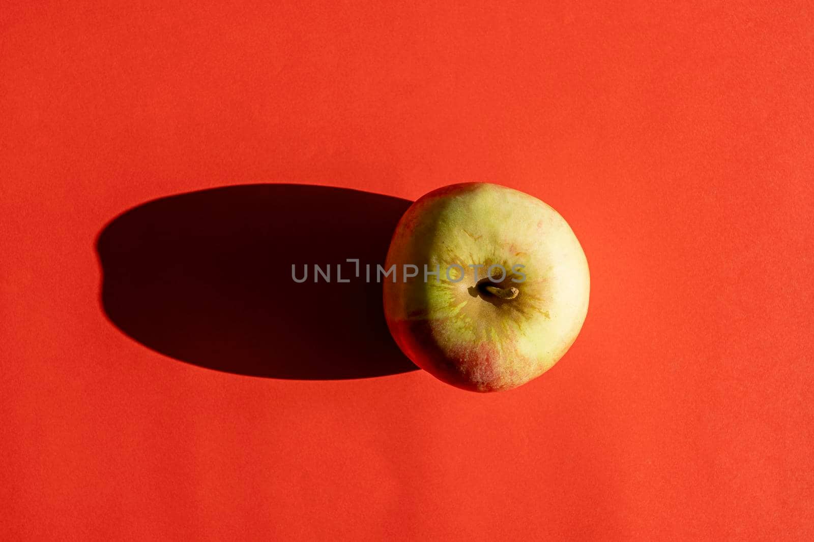 an apple with a hard shadow on a red background. photo