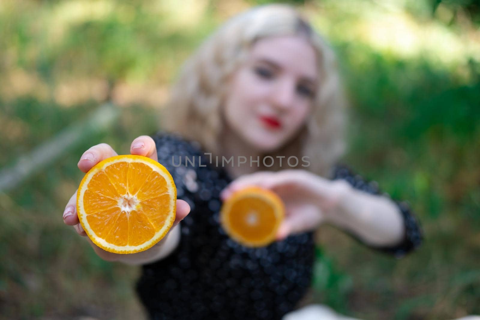 portrait of a charming blonde teenage girl with a fresh orange outdoors in forest or park. tasty juicy fruit.