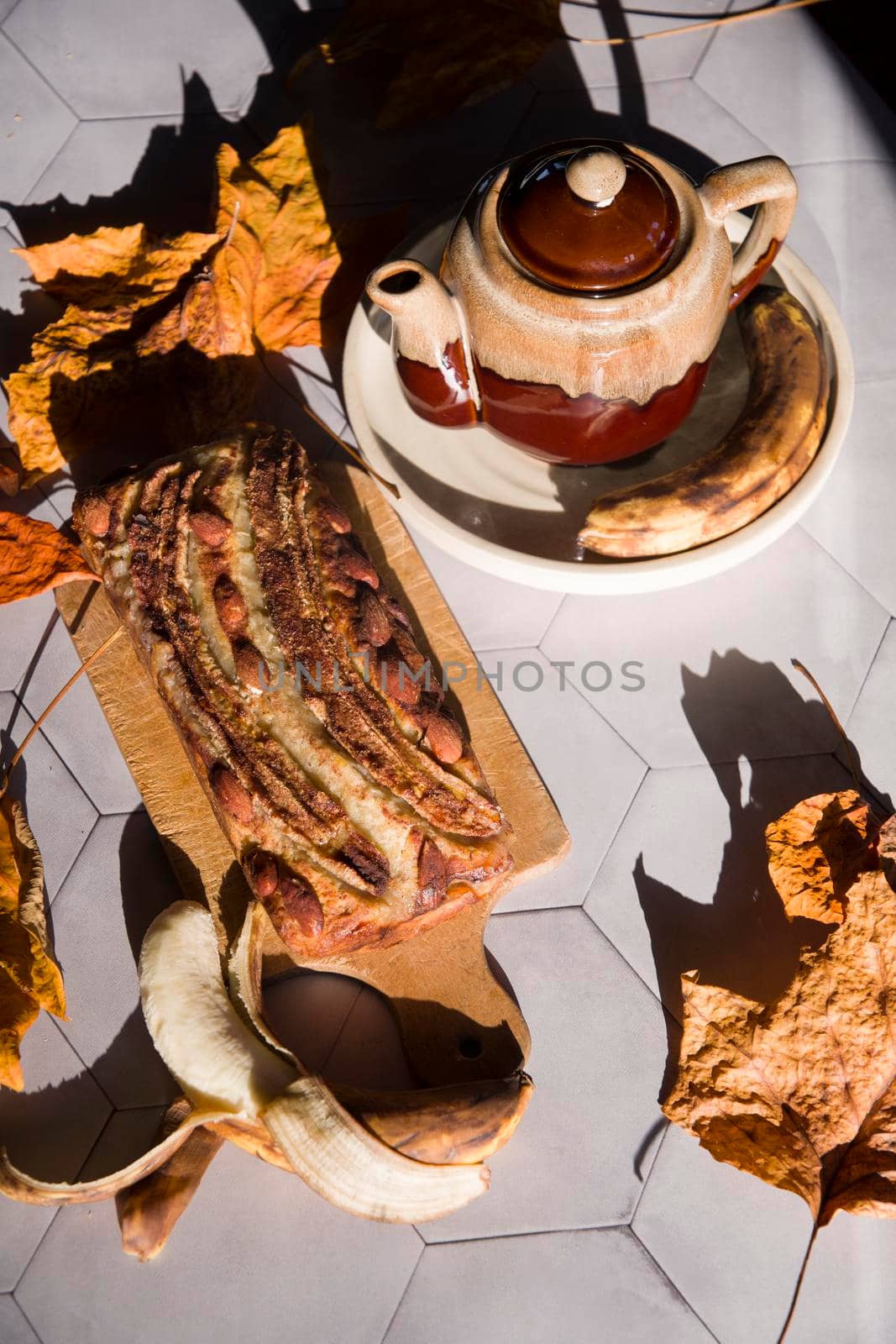 Still life Banana pie with a ceramic teapot in the rays of the autumn sun on a gray tile table. High quality photo
