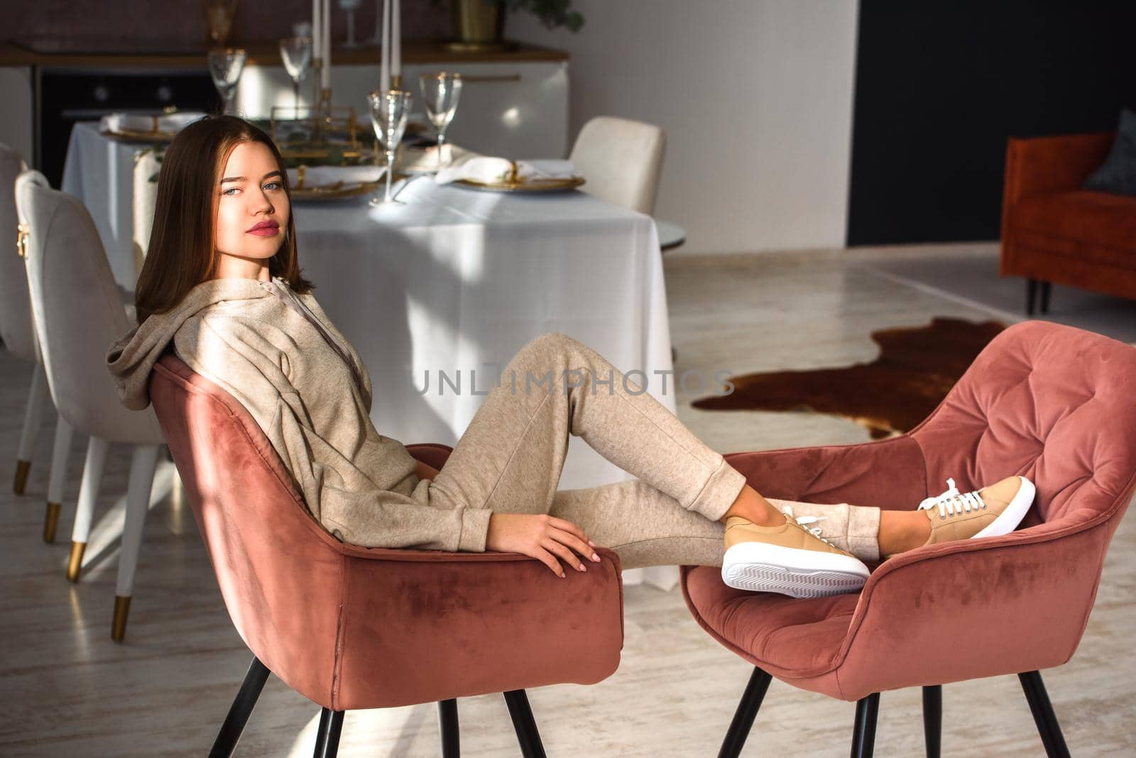 photo of a women in beige sports suit and stylish leather sneakers posing in the chair on a kitchen . selective focus. Indoors