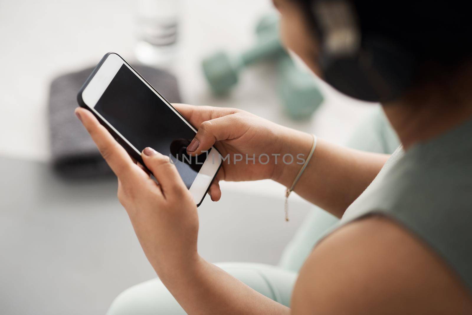 Closeup shot of an unrecognisable woman using a cellphone while exercising at home.