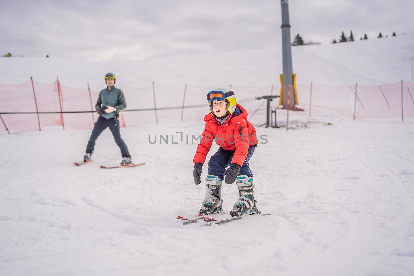 Boy learning to ski, training and listening to his ski instructor on the slope in winter.