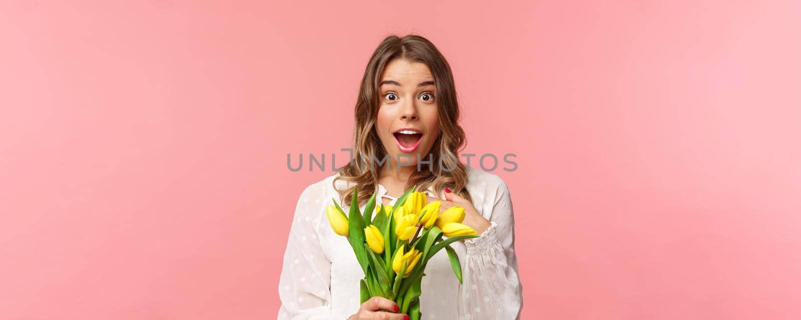 Spring, happiness and celebration concept. Close-up of surprised and wondered young blond girl in white dress, receive yellow tulips and pointing herself with disbelied and amazement, didnt expact.