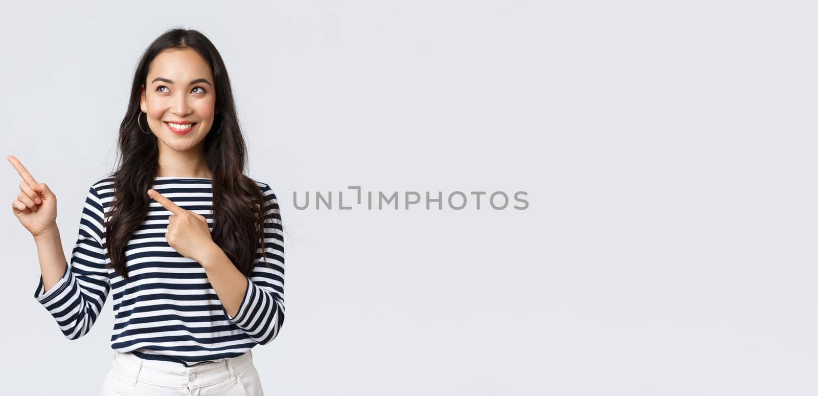 Lifestyle, people emotions concept. Excited good-looking asian girl smiling pleased as found excellent product, pointing fingers left at advertisement and looking satisfied, recommend promo.