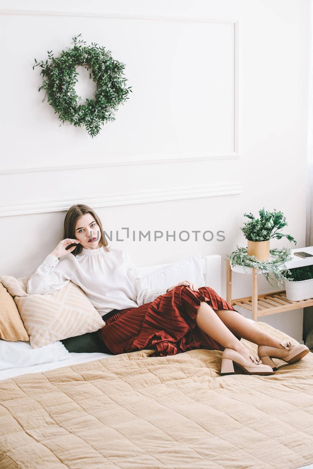 Portrait of fashionable women in red skirt, white blouse and stylish beige high-heeled shoes with a chain buckle posing in a bed. Girl with a big red lips