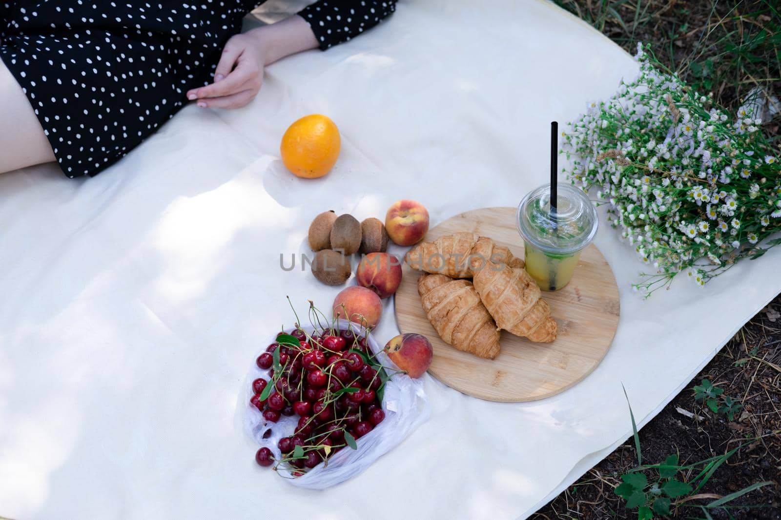 Healthy picnic for a summer day with croissants, fresh fruits and lemonade. peach, cherry, kiwi, oranges. white wildflowers.