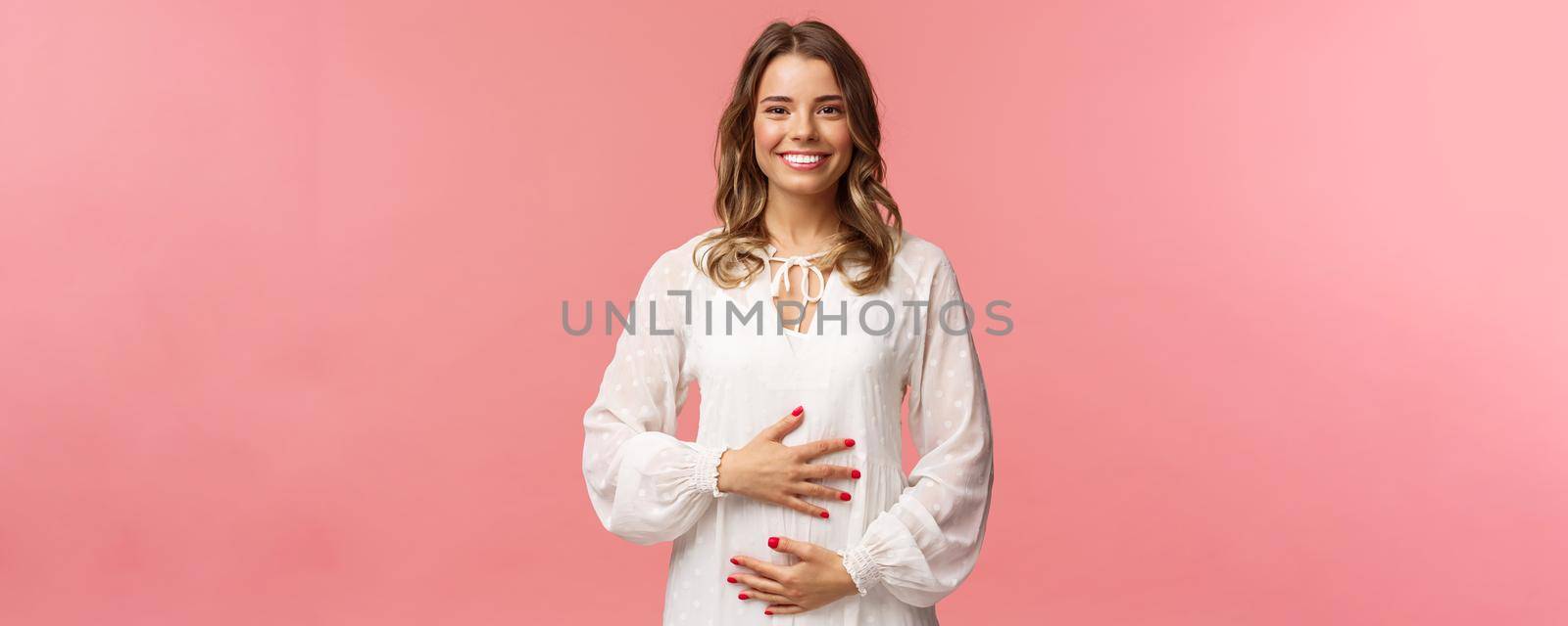 Pregnancy, women and beauty concept. Happy tender and cute blond young woman, wife expecting child, holding hands on belly pleased, smiling camera, surprise husband with awesome news by Benzoix