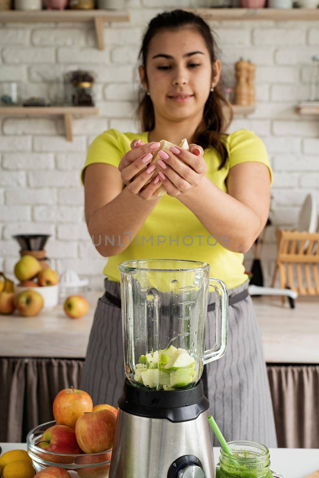 Preparing healthy foods. Healthy eating and dieting. Young brunette woman making banana smoothie at home kitchen