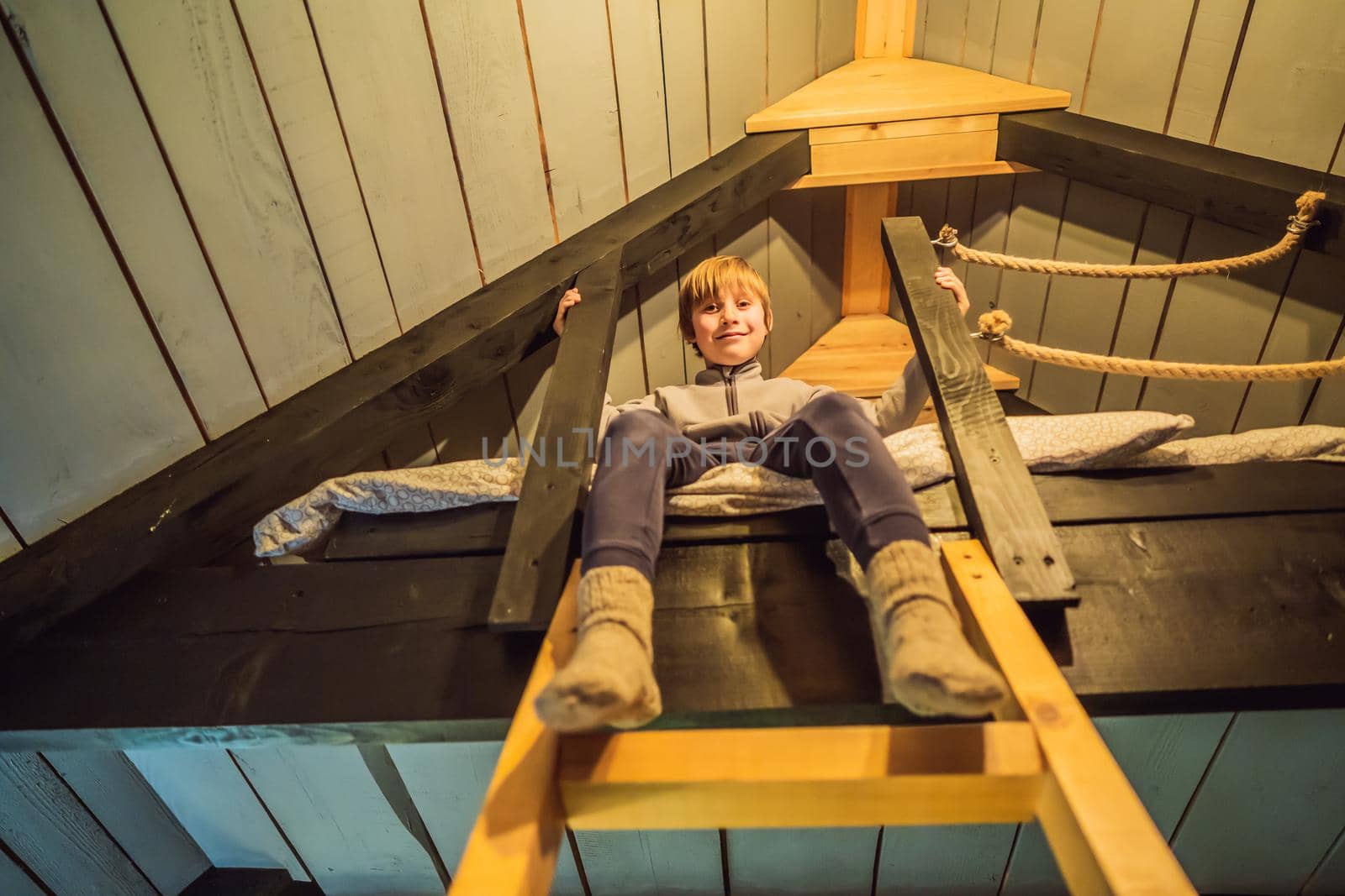 A boy sits on a bed on the 2nd floor in a glamping. Rest in the mountains in Glamping. Cozy house in a mountain by galitskaya