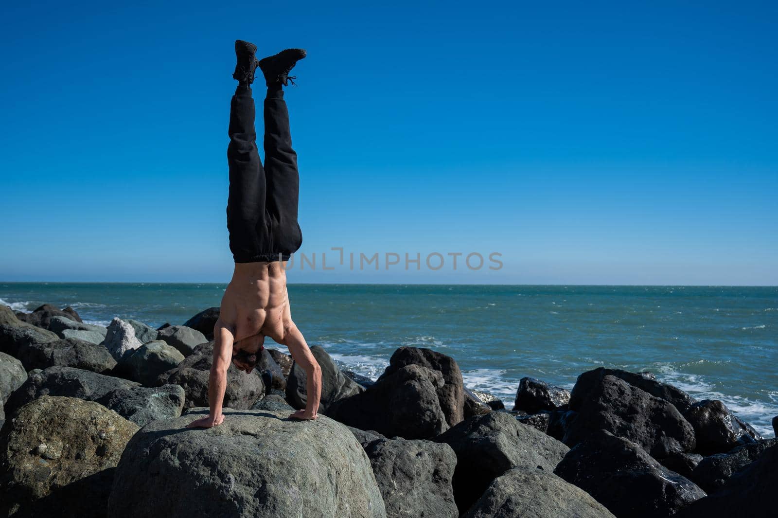 Shirtless man doing handstand on rocks by the sea. by mrwed54