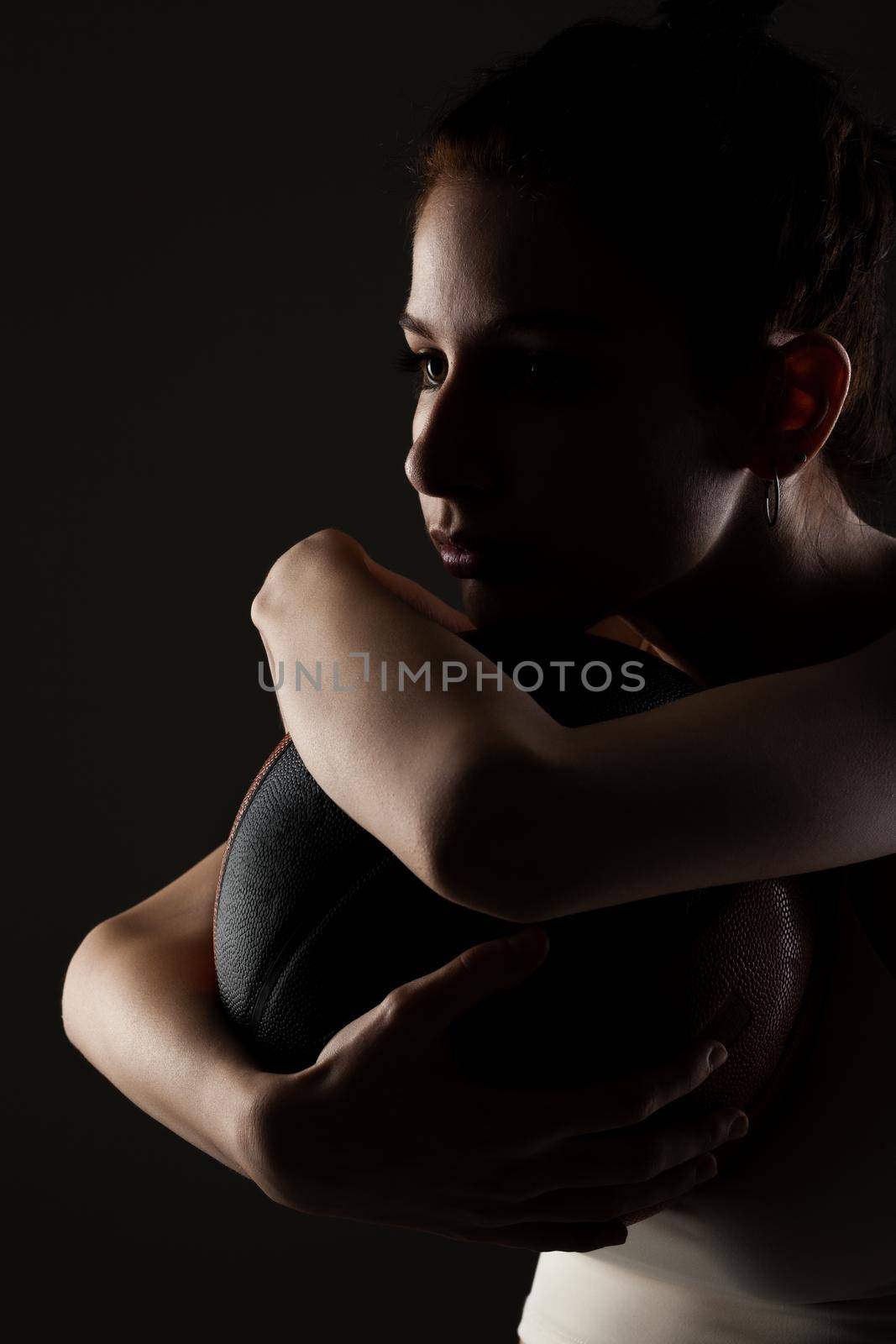 Teenage girl with basketball. Side lit studio portrait against dark background.. by kokimk