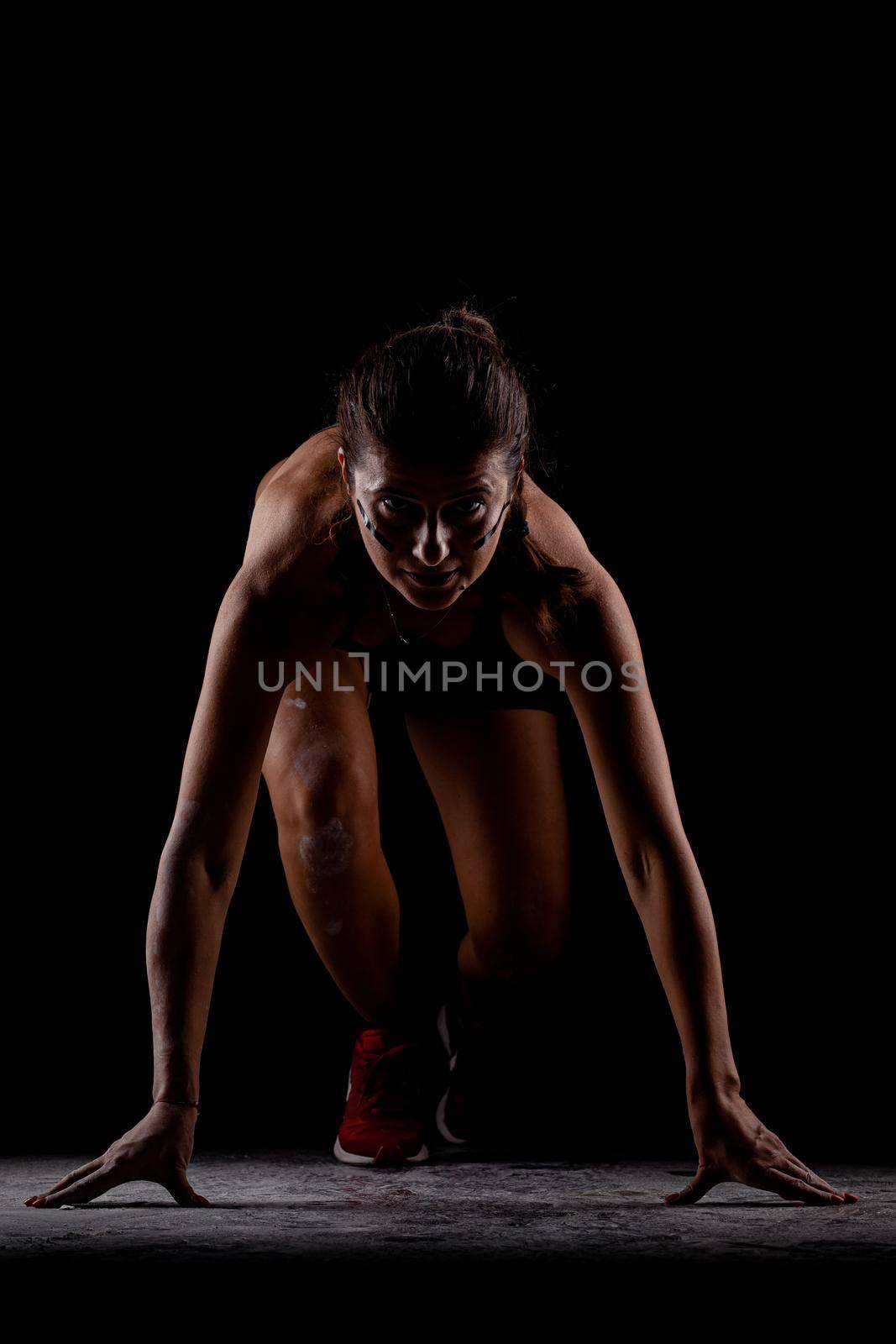 Side lit silhouette fit girl in race start position against dark background.. by kokimk