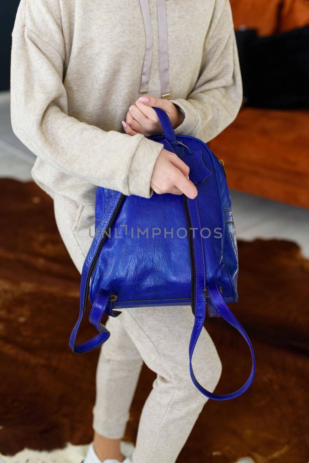 photo of a blue leather backpack in womens hand. Girl wearing beige sports suit. selective focus by Ashtray25