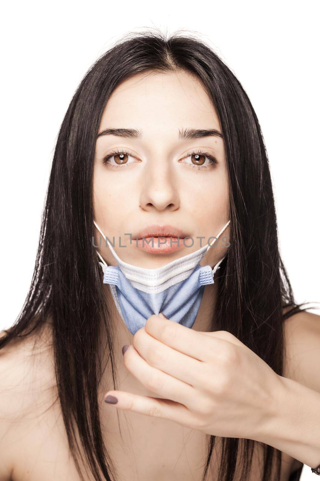 Serious looking girl pulling away medical face mask. Portrait against white background.