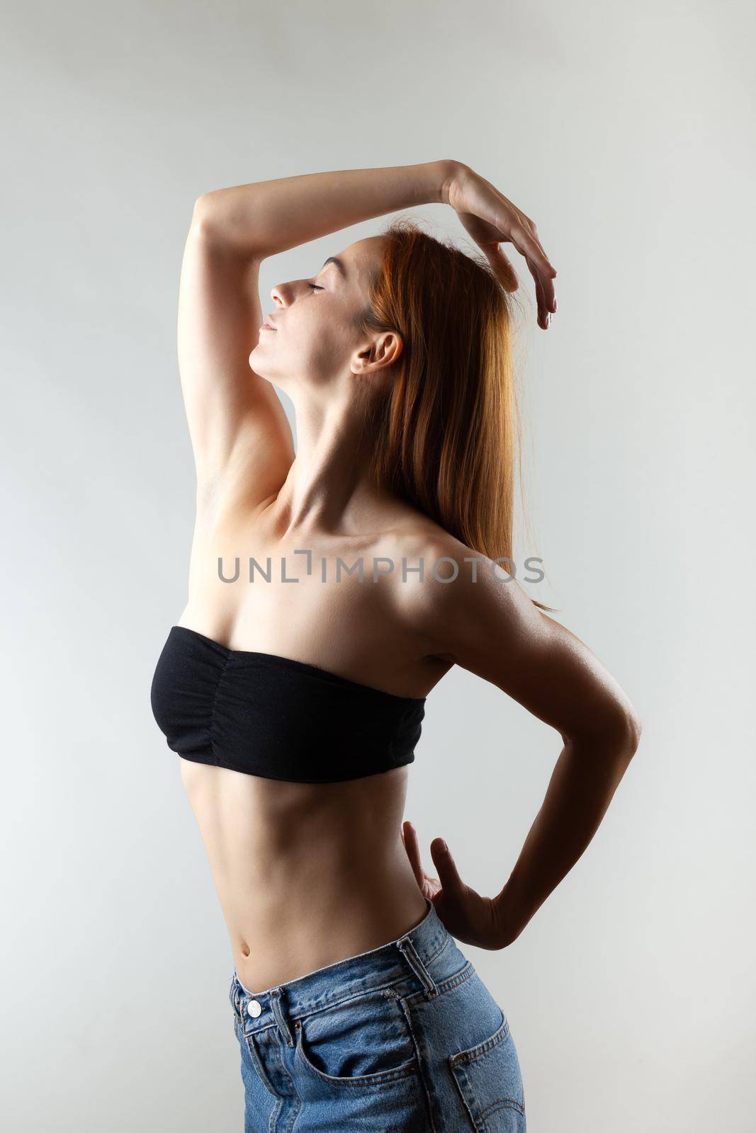 Beautiful girl with burnt orange hair stretching and making ballet pose. Studio portrait on gray background.
