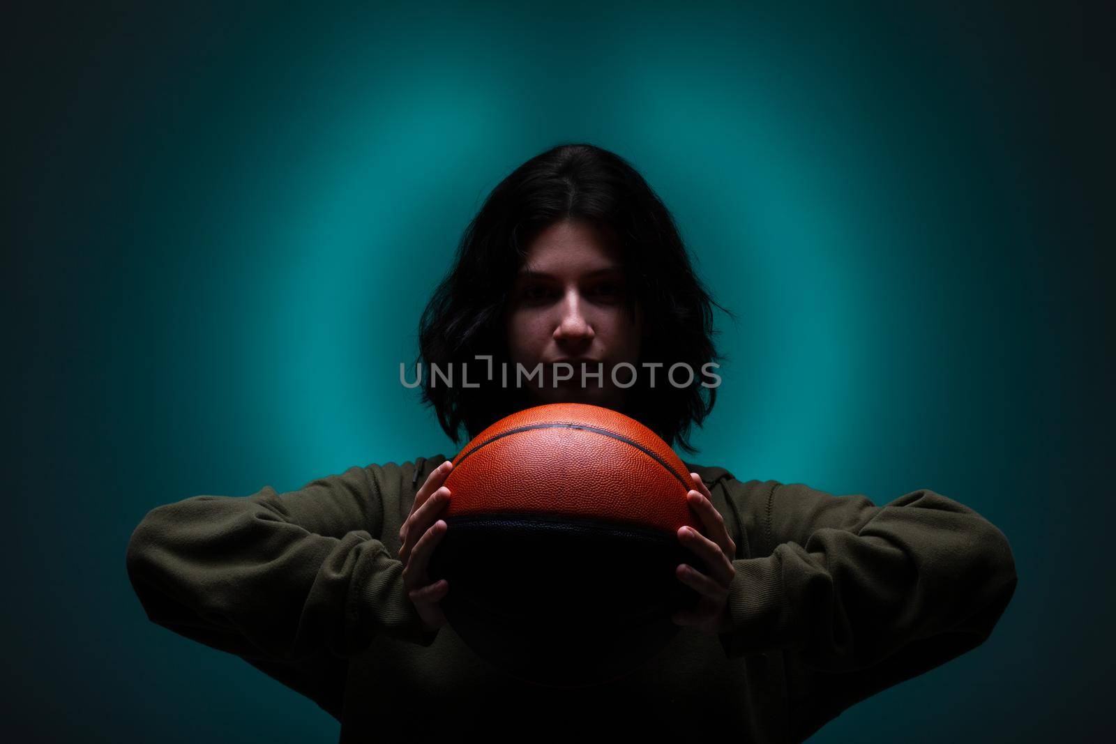 Teenage girl with basketball. Studio portrait with neon blue colored background.