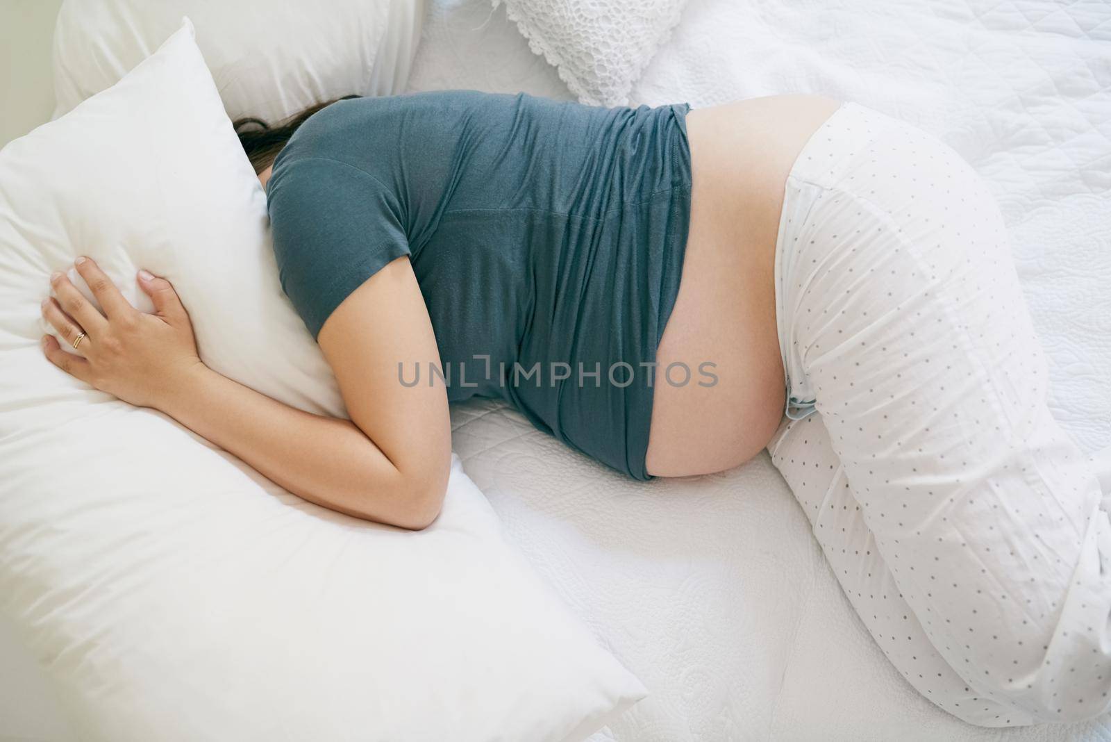 I just want sleep and more sleep. Shot of a pregnant woman lying with her head under her pillow. by YuriArcurs