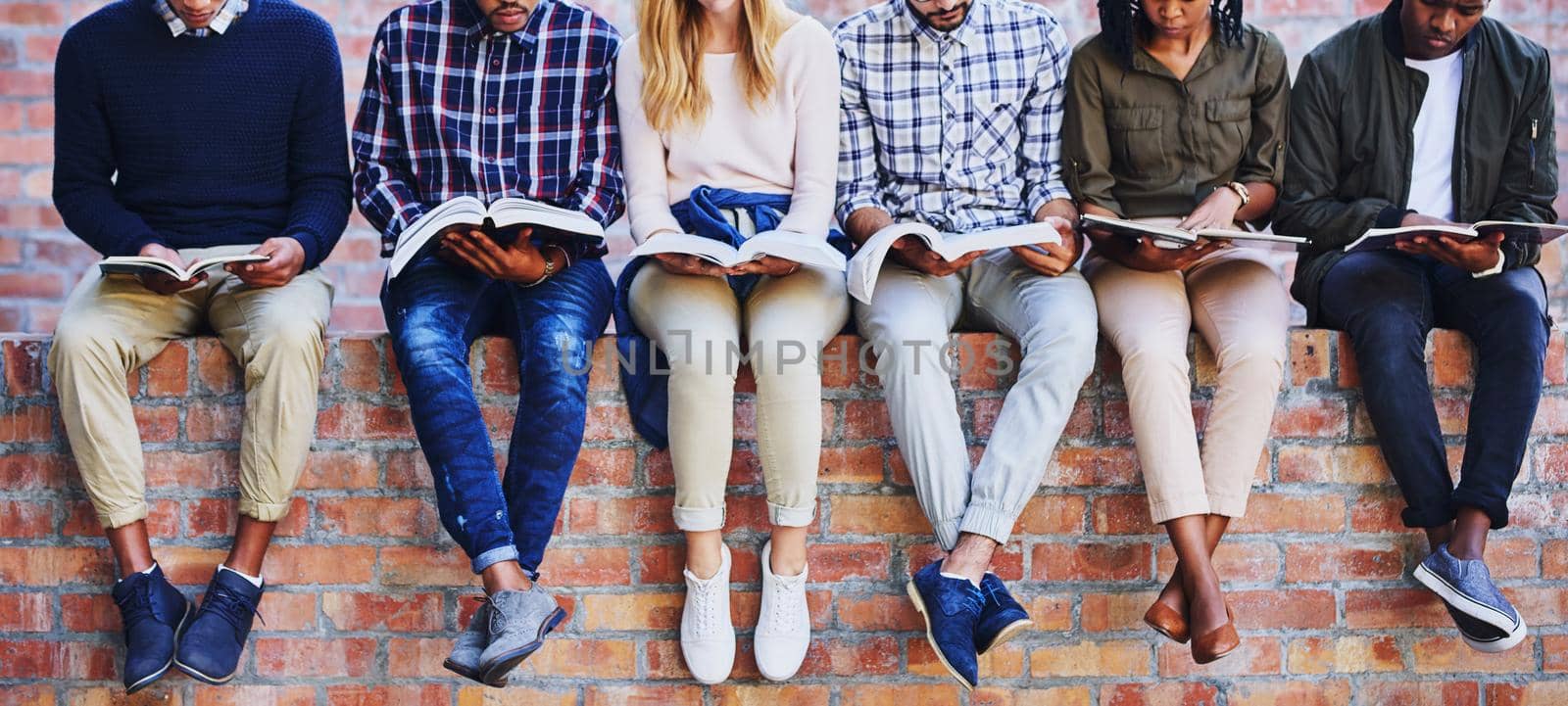 Studying on campus. Cropped shot of a group of unrecognizable university students studying while sitting outside on a facebrick wall. by YuriArcurs