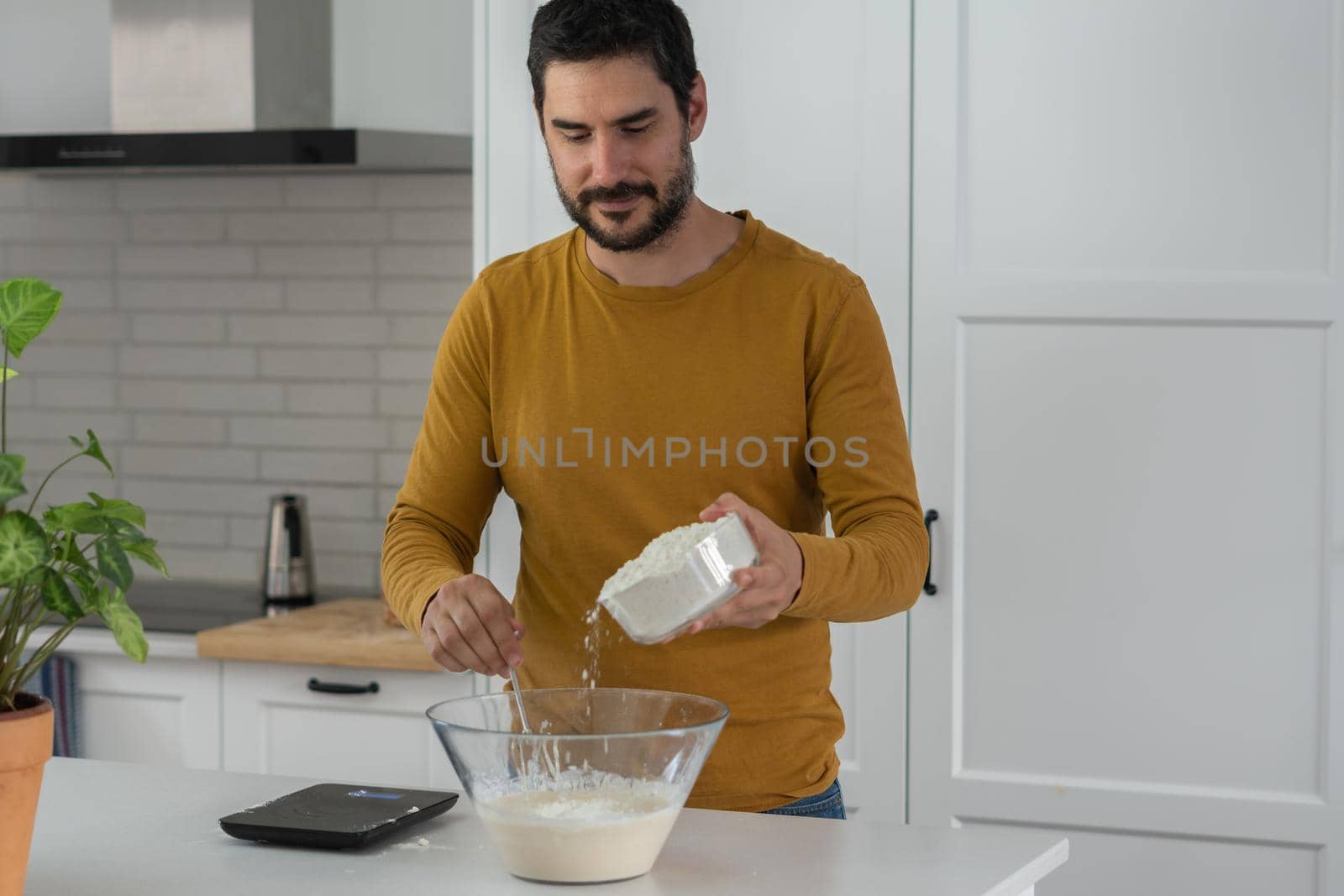 young man making bread in the kitchen of his home by joseantona