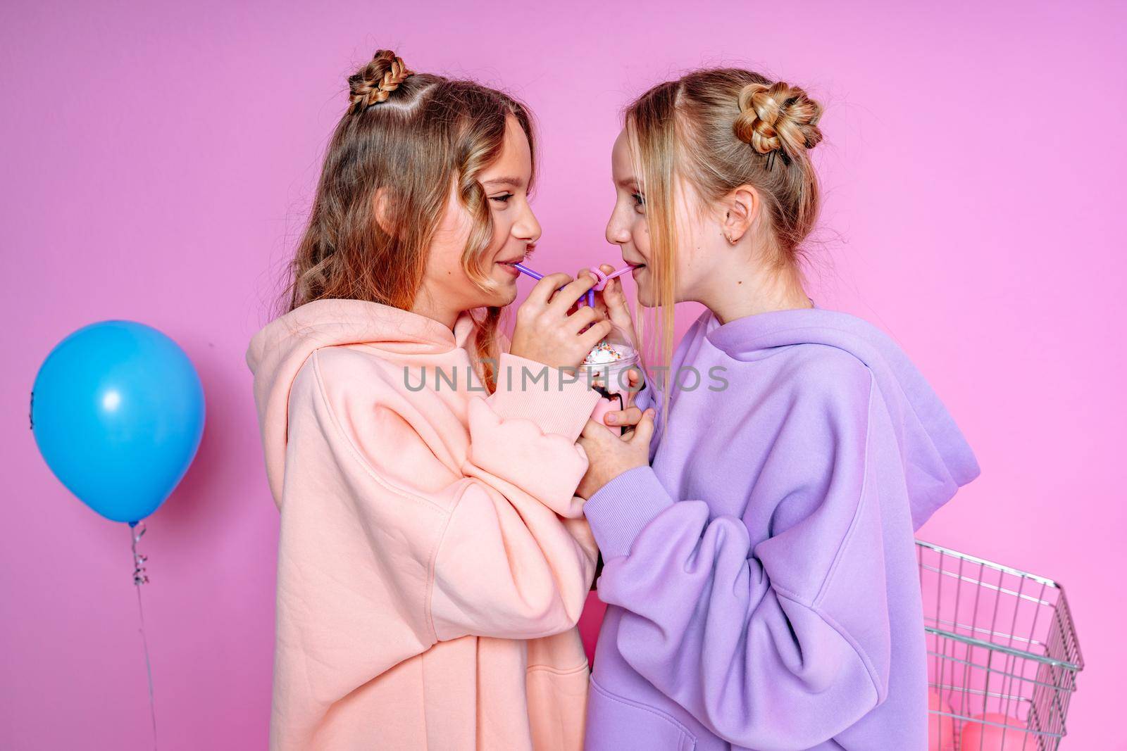 Two beautiful attractive funny joyful cheerful relaxed carefree girls dressed in casual fashion clothes isolated on hot pink background by Matiunina
