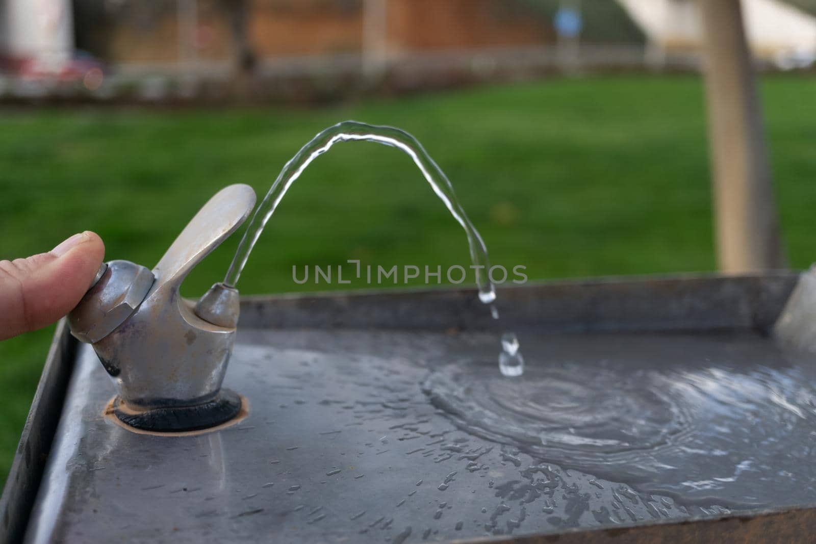 hand in the foreground opening the tap of a fountainfocused background and water falling splash