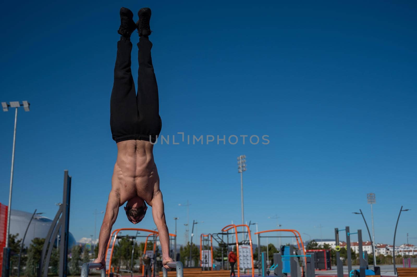 Shirtless man doing handstand on parallel bars at sports ground