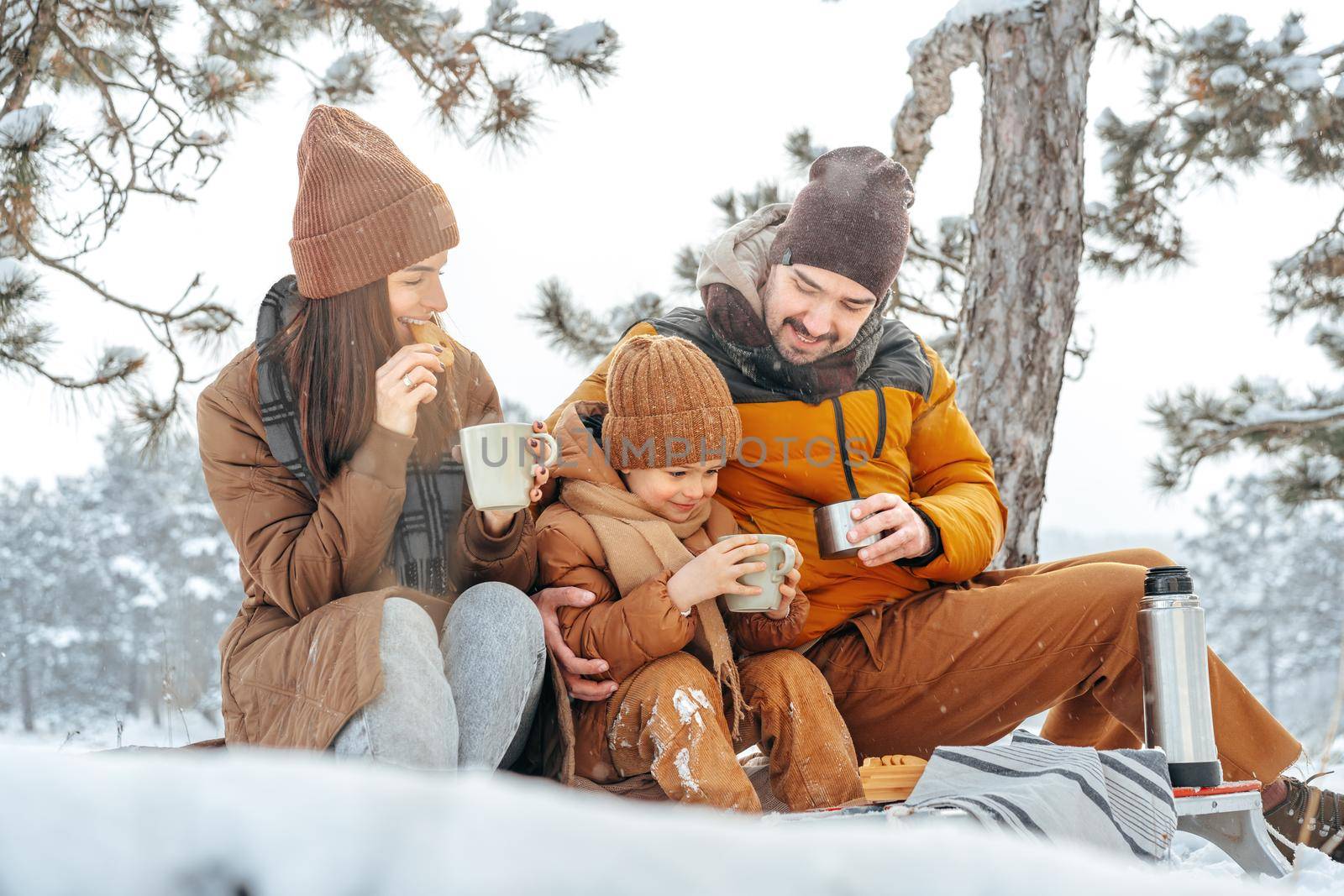 Happy family with cups of hot tea spending time together in winter forest, close up