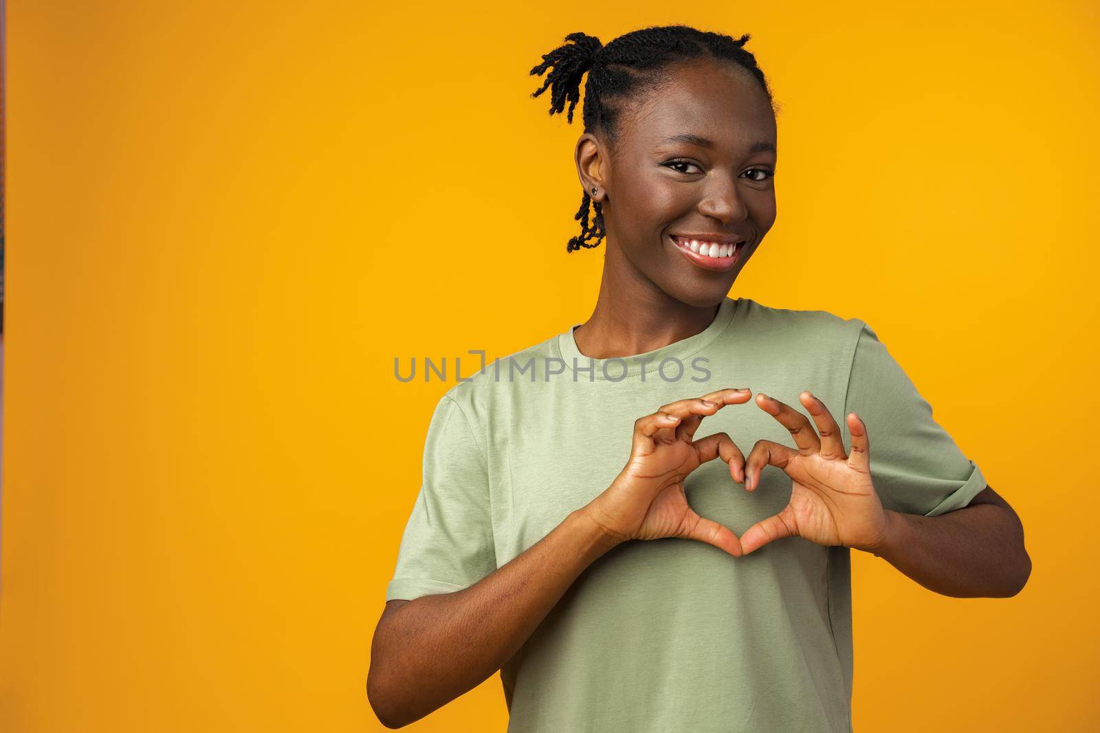 Young african american woman smiling and showing a heart shape with hands in yellow studio