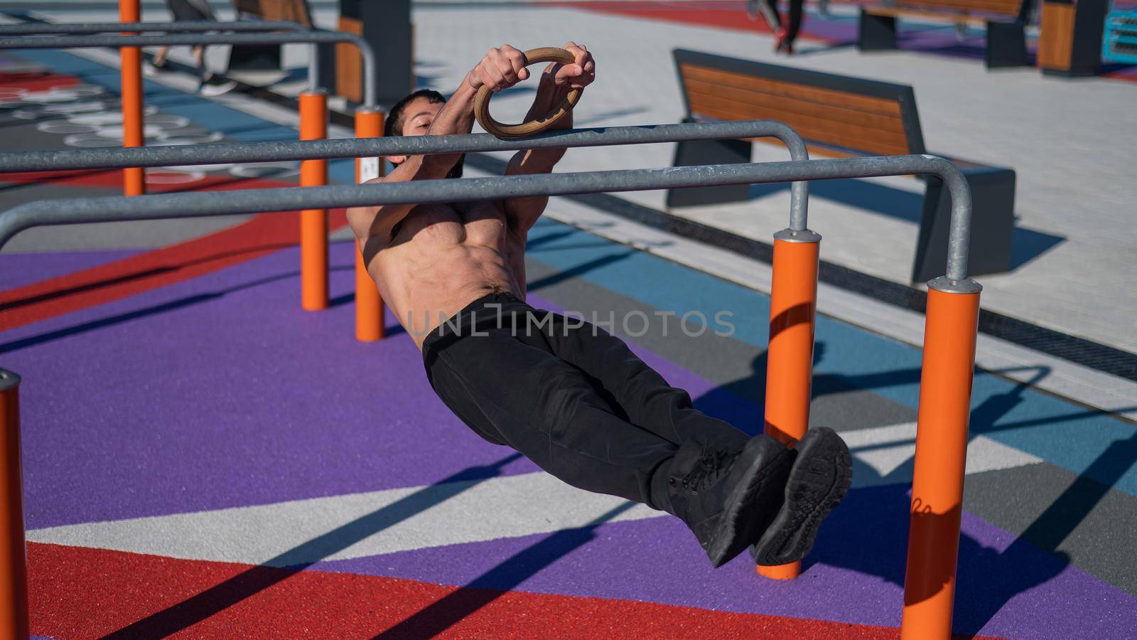 Shirtless man doing horizontal balance on parallel bars at sports ground. by mrwed54
