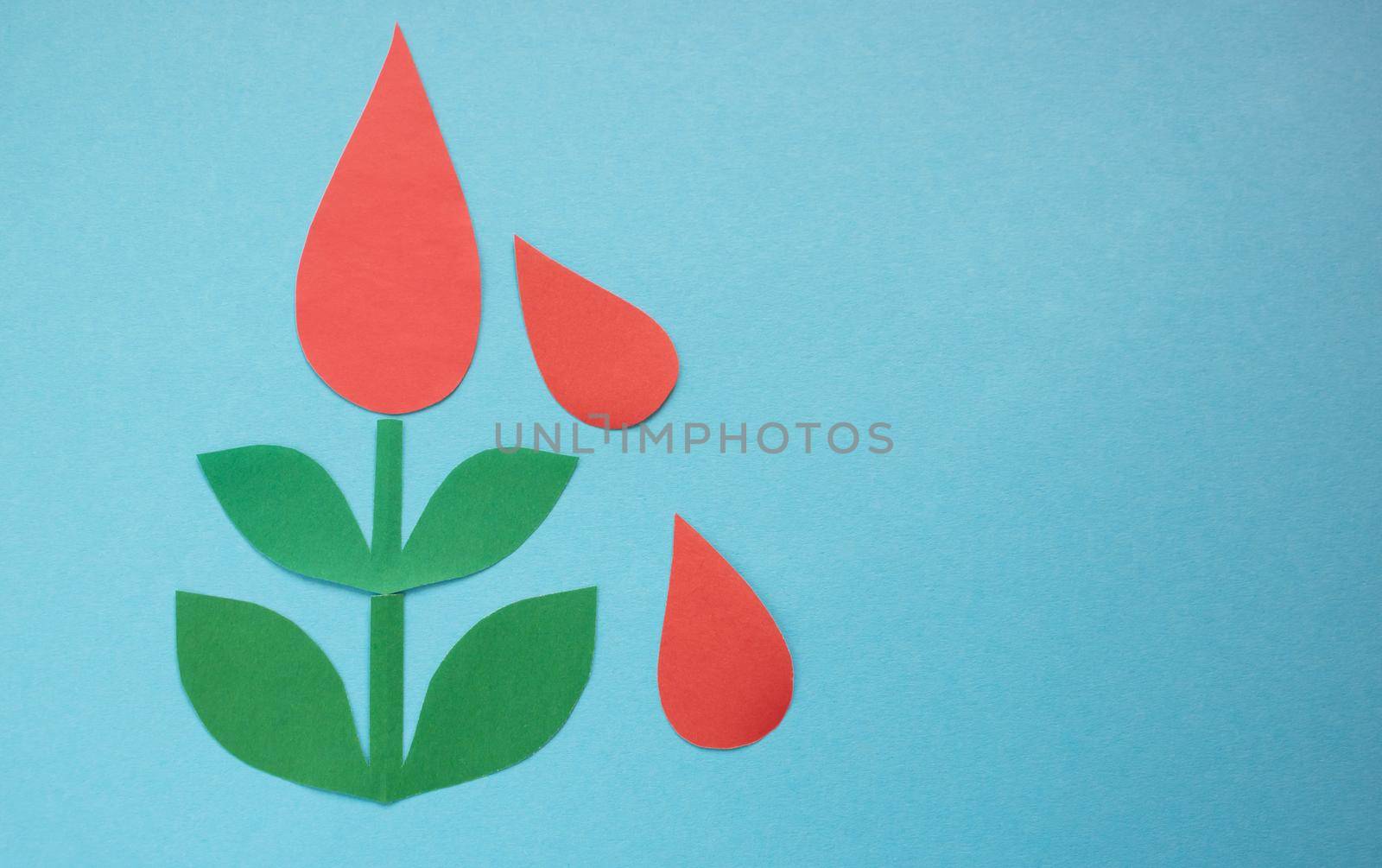 Drops of blood from paper on a green tree on a blue background.The concept of the World Blood Donor and Hemophilia Day.