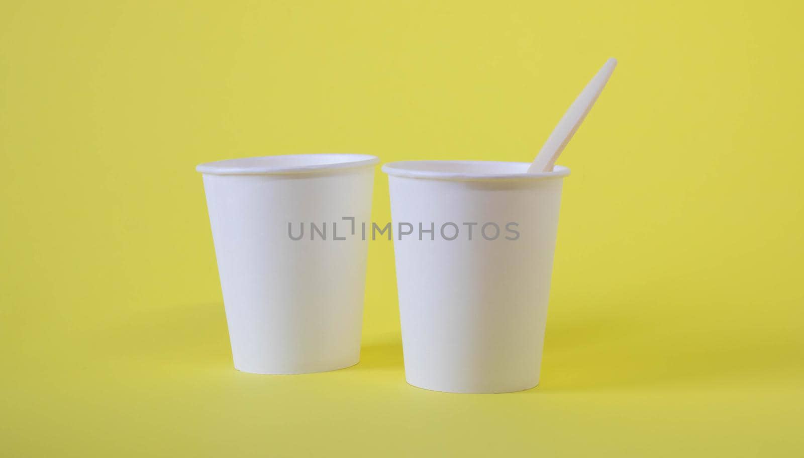 Two small white paper cups on a yellow background by lapushka62