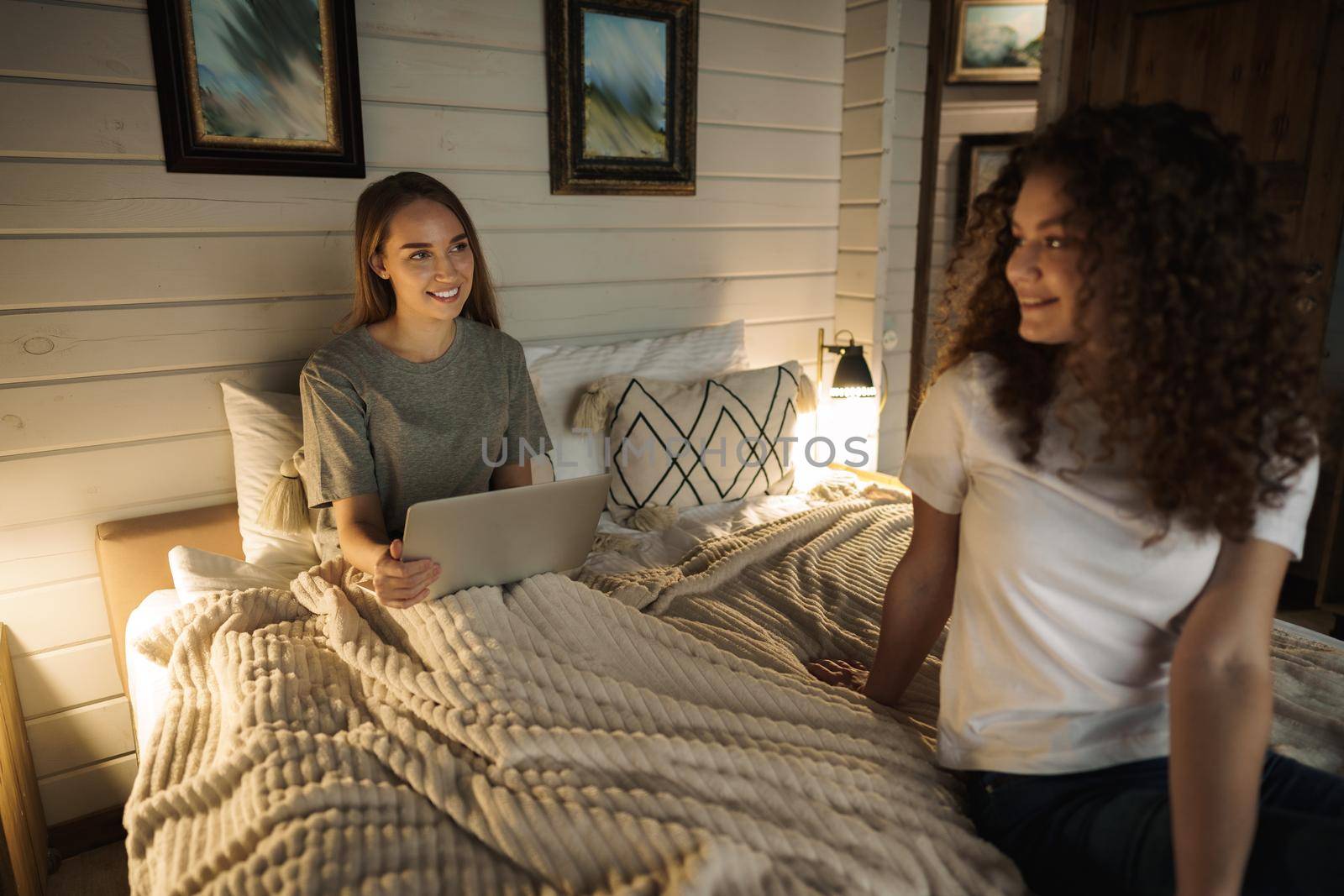 Two beautiful women lying in bed, holding and watching laptop